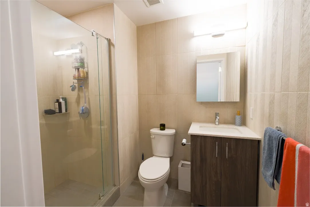 Full bath with vanity, tile walls, light tile patterned floors, and a shower stall