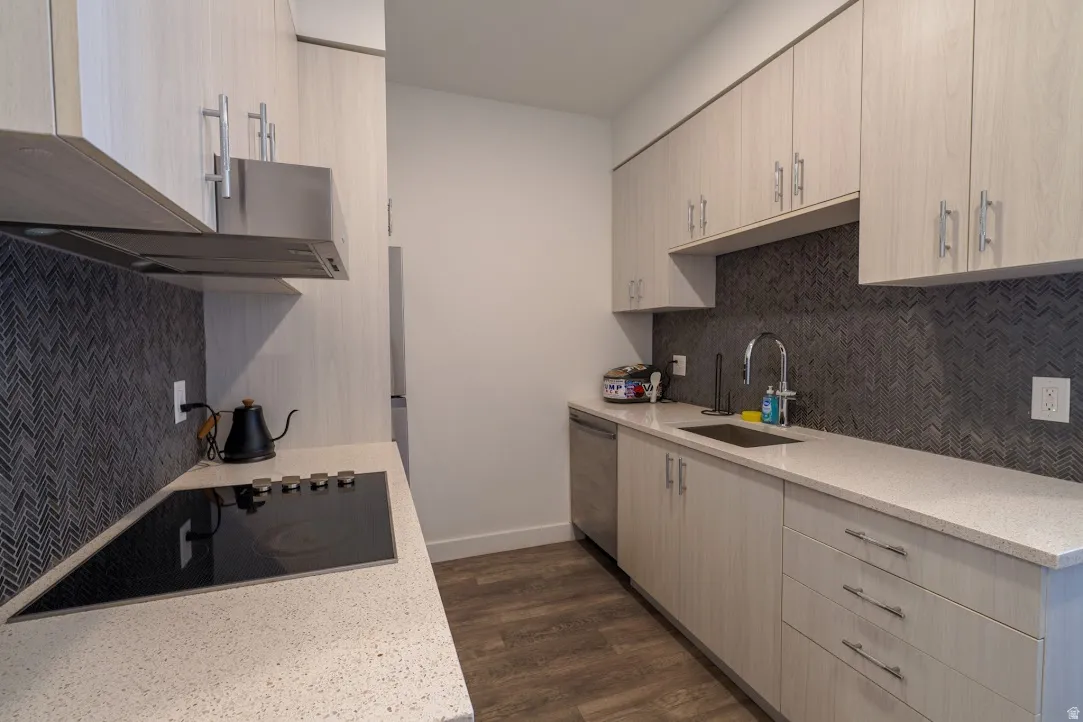 Kitchen featuring dark wood-style floors, light stone countertops, black electric cooktop, dishwasher, and light wood finish cabinetry