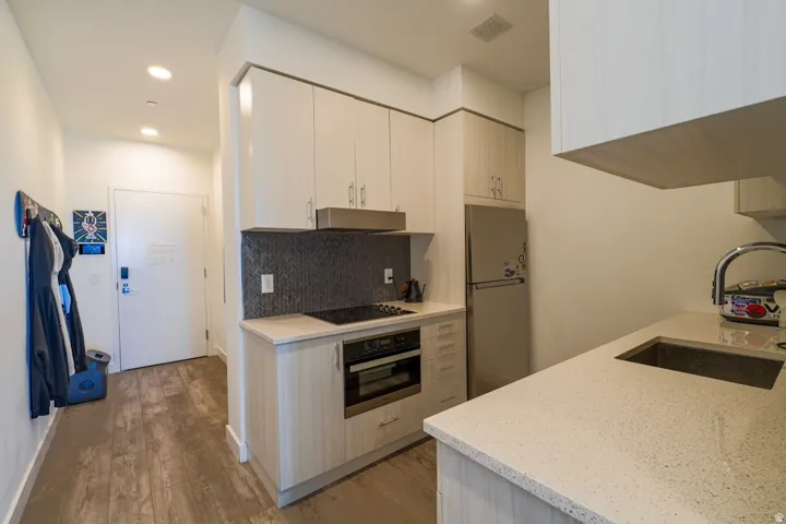 Kitchen featuring light stone counters, freestanding refrigerator, wall oven, light wood-style floors, and backsplash