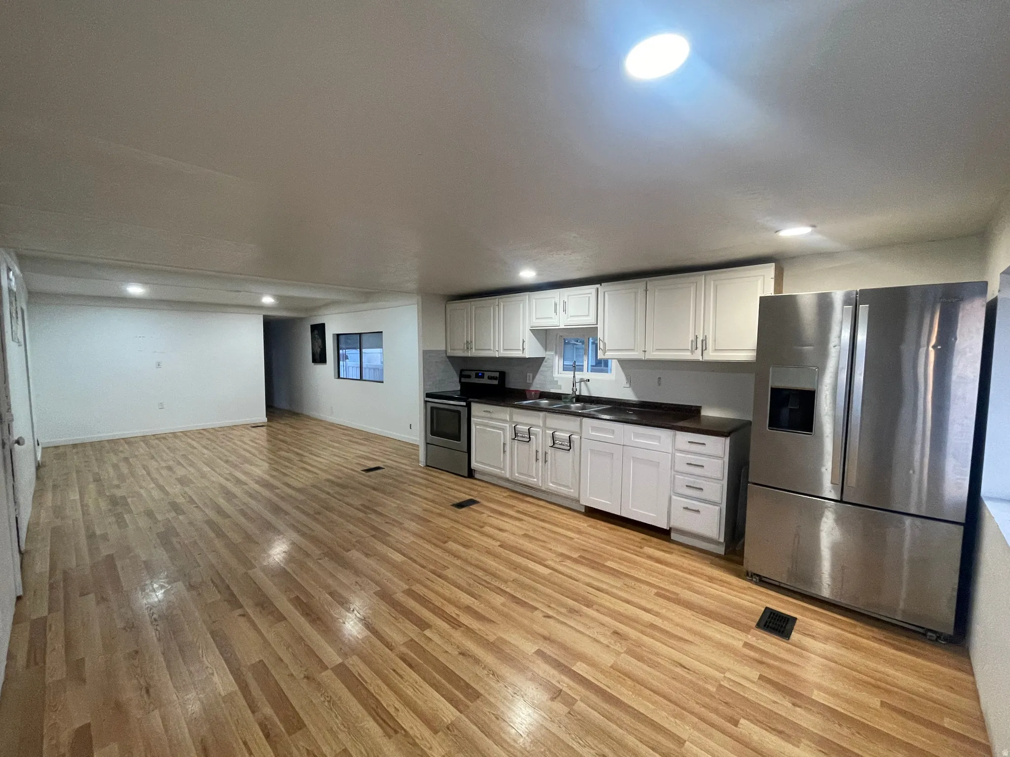 Kitchen featuring dark countertops, stainless steel appliances, white cabinets, light wood-type flooring, and recessed lighting