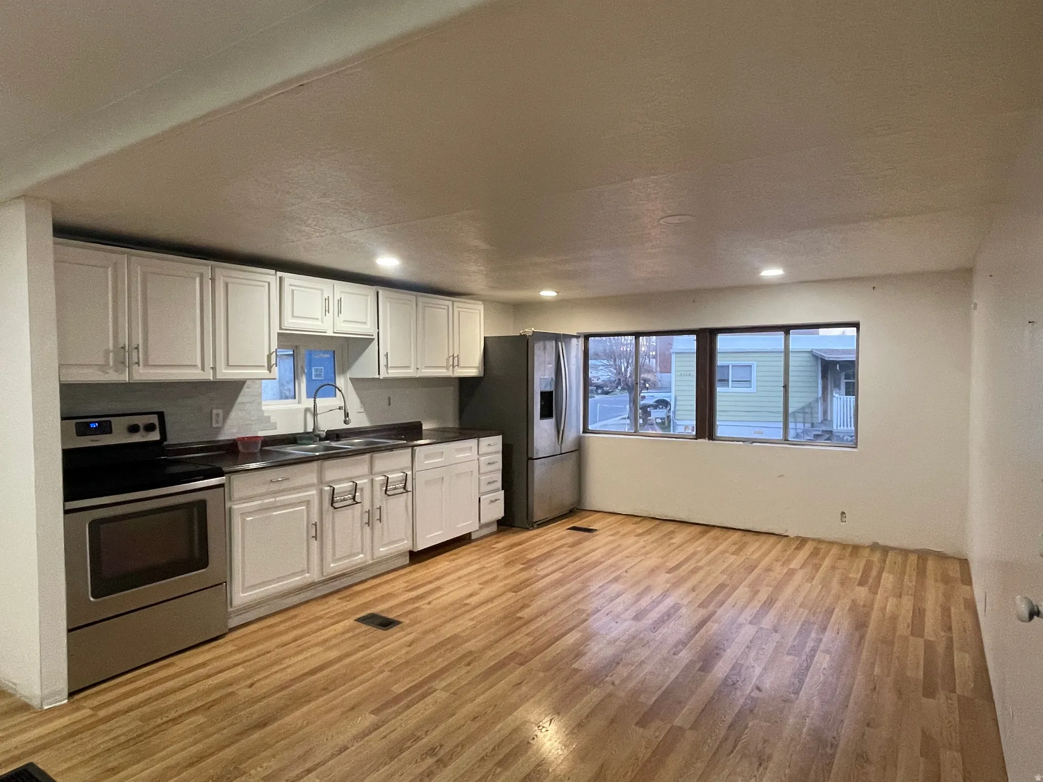 Kitchen with stainless steel appliances, dark countertops, white cabinetry, light wood finished floors, and recessed lighting