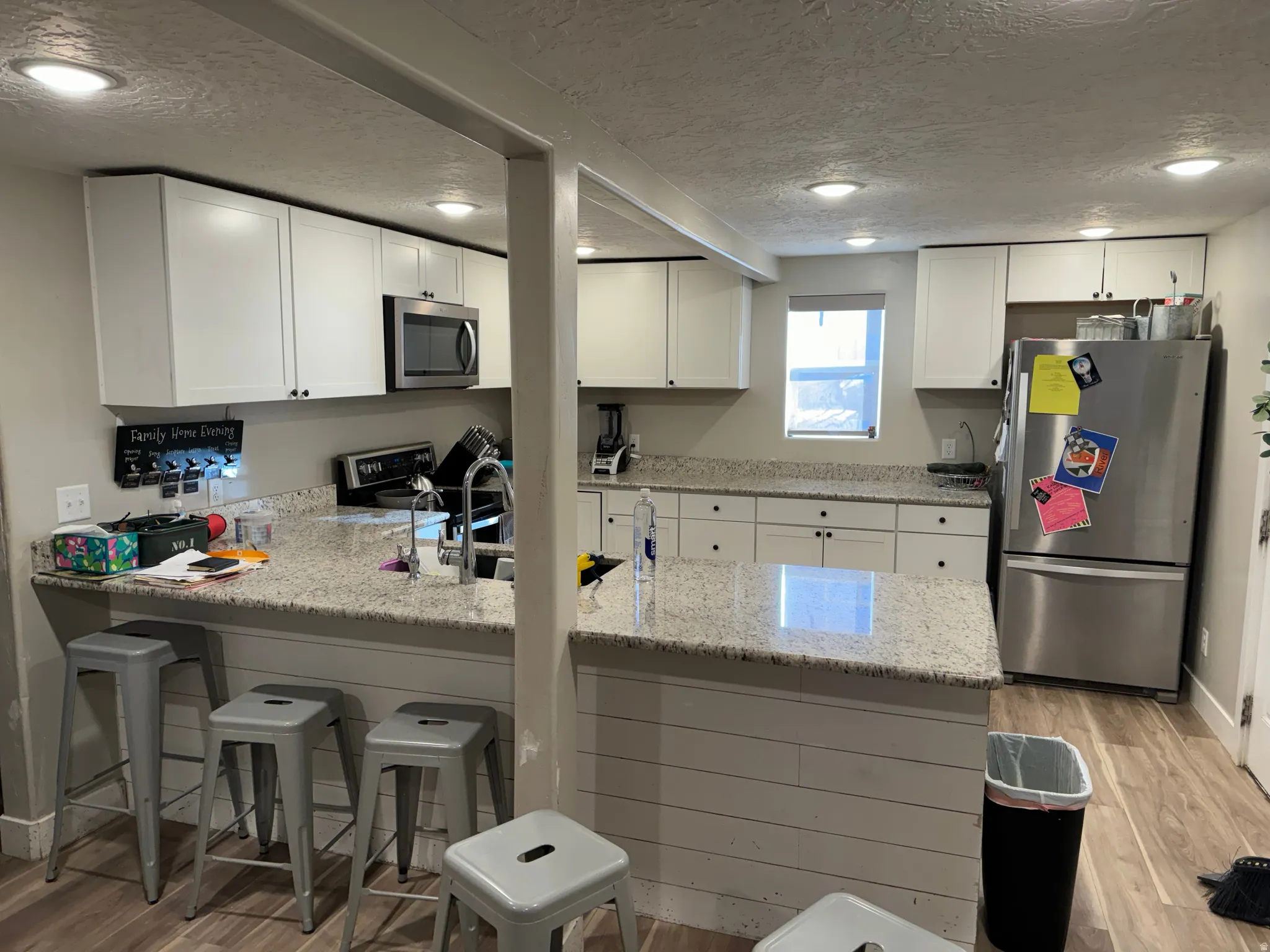 Kitchen featuring a peninsula, light wood finished floors, a textured ceiling, stainless steel appliances, and a breakfast bar area