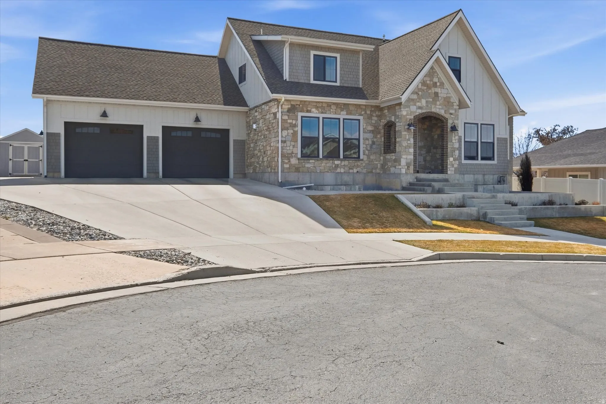 View of front facade featuring stone siding, a shingled roof, driveway, and a garage