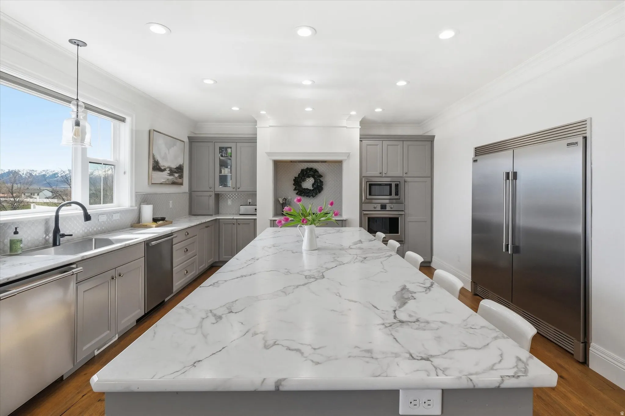 Kitchen with gray cabinets, built in appliances including full size fridge and freezer, 2 dishwashers, gas range,  a kitchen bar, and ornamental molding