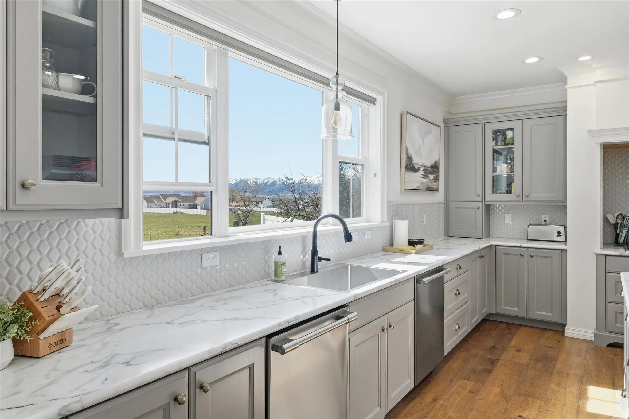 Kitchen featuring glass fronted cabinets, gray cabinets, stainless steel dishwasher, tasteful backsplash, and dark wood-style floors