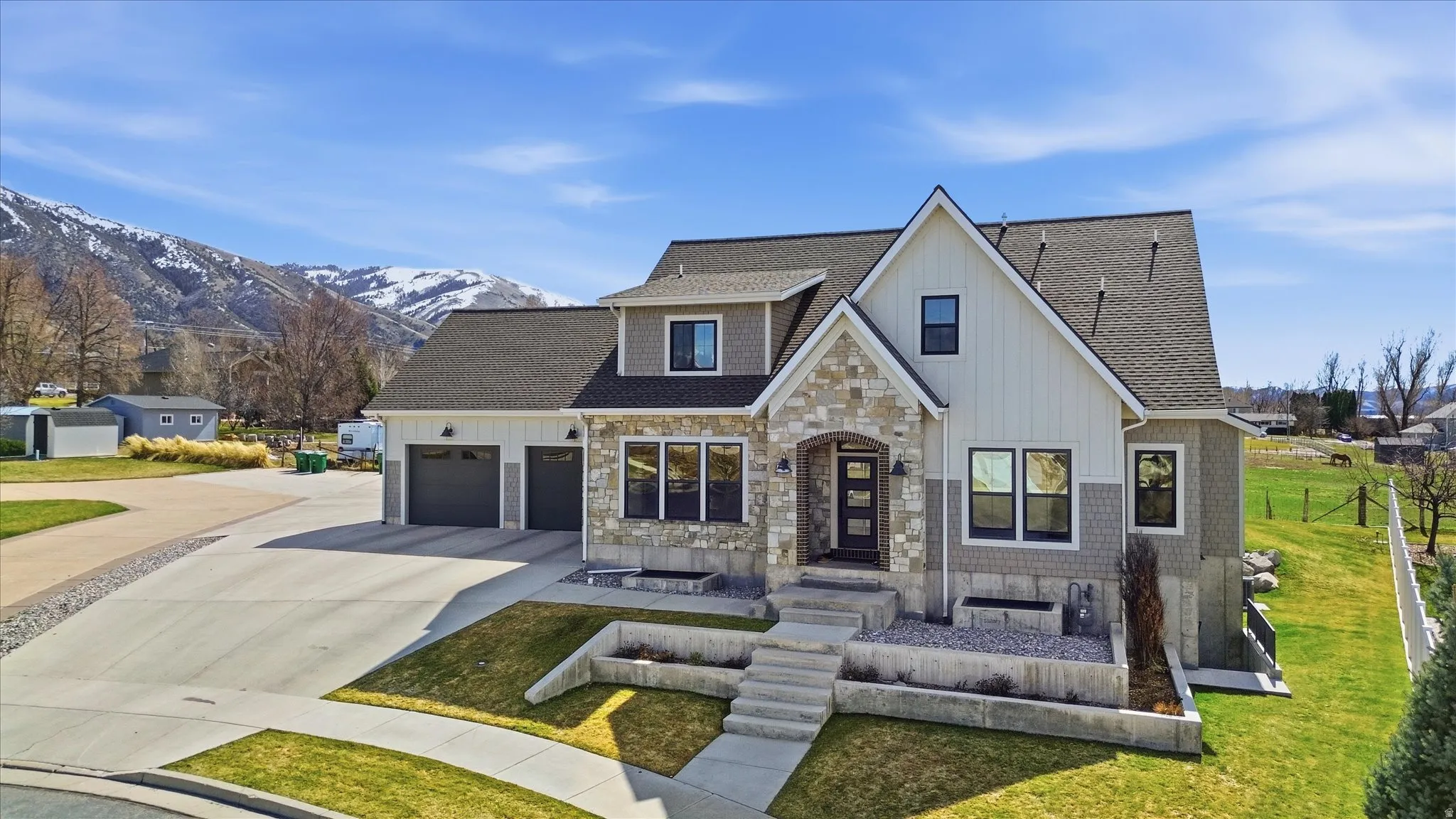 View of front of house featuring stone siding, roof with shingles, concrete driveway, an attached garage, and a front yard