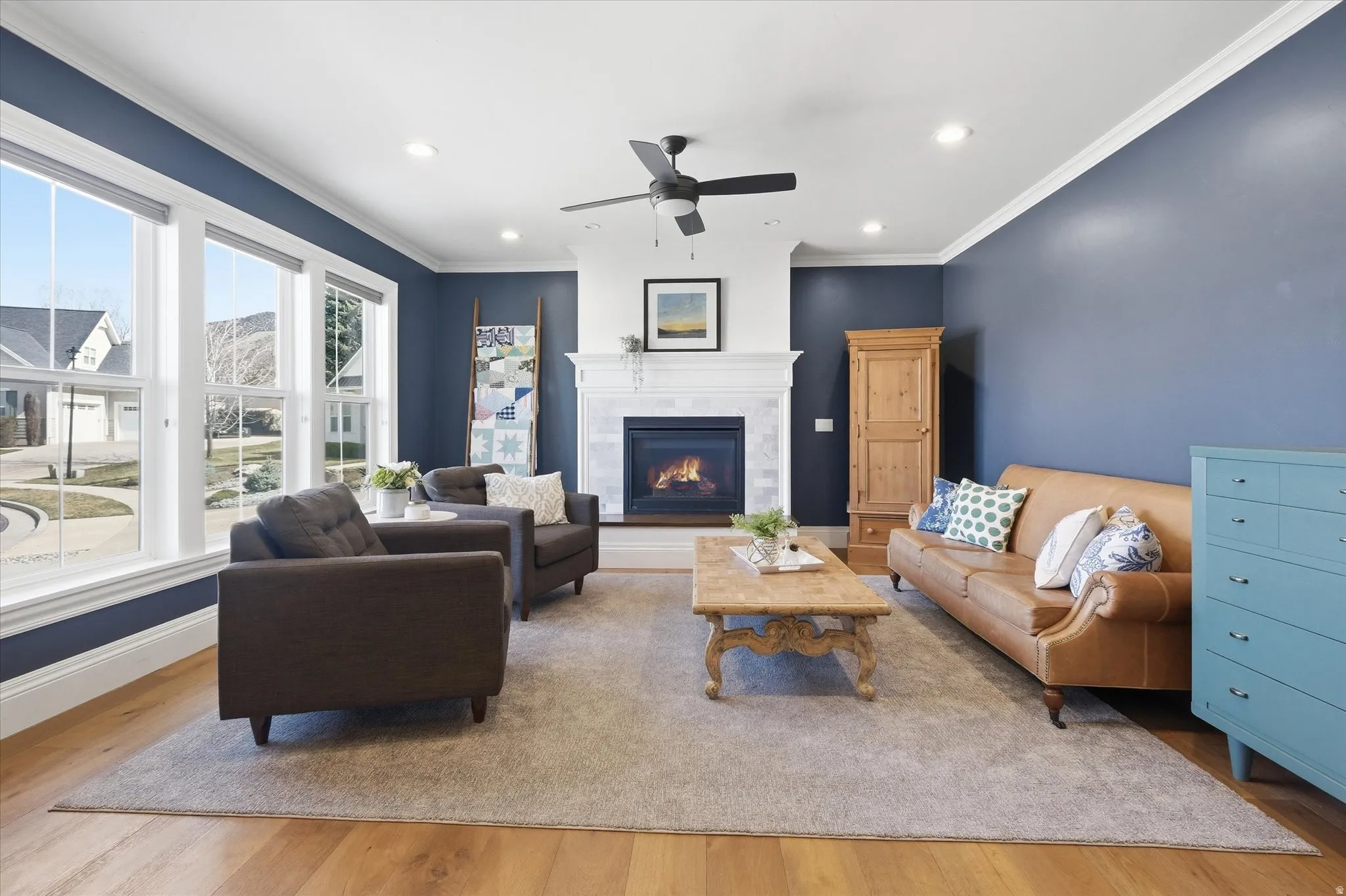 Living area with light wood finished floors,gas fireplace, ceiling fan, recessed lighting, and ornamental molding