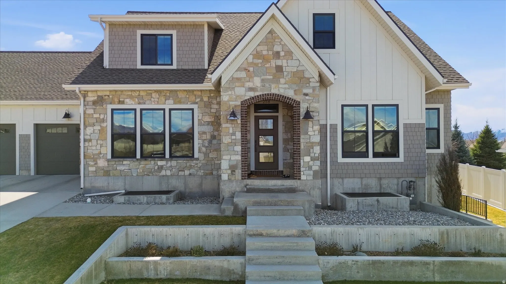View of front of property featuring stone siding, roof with shingles, board and batten siding, concrete driveway, and a garage