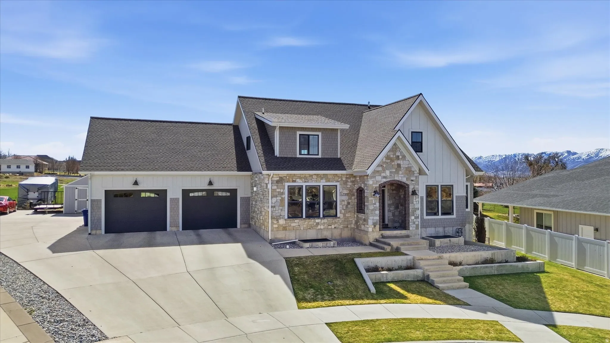 View of front facade with stone siding, roof with shingles, a garage, concrete driveway, and board and batten siding