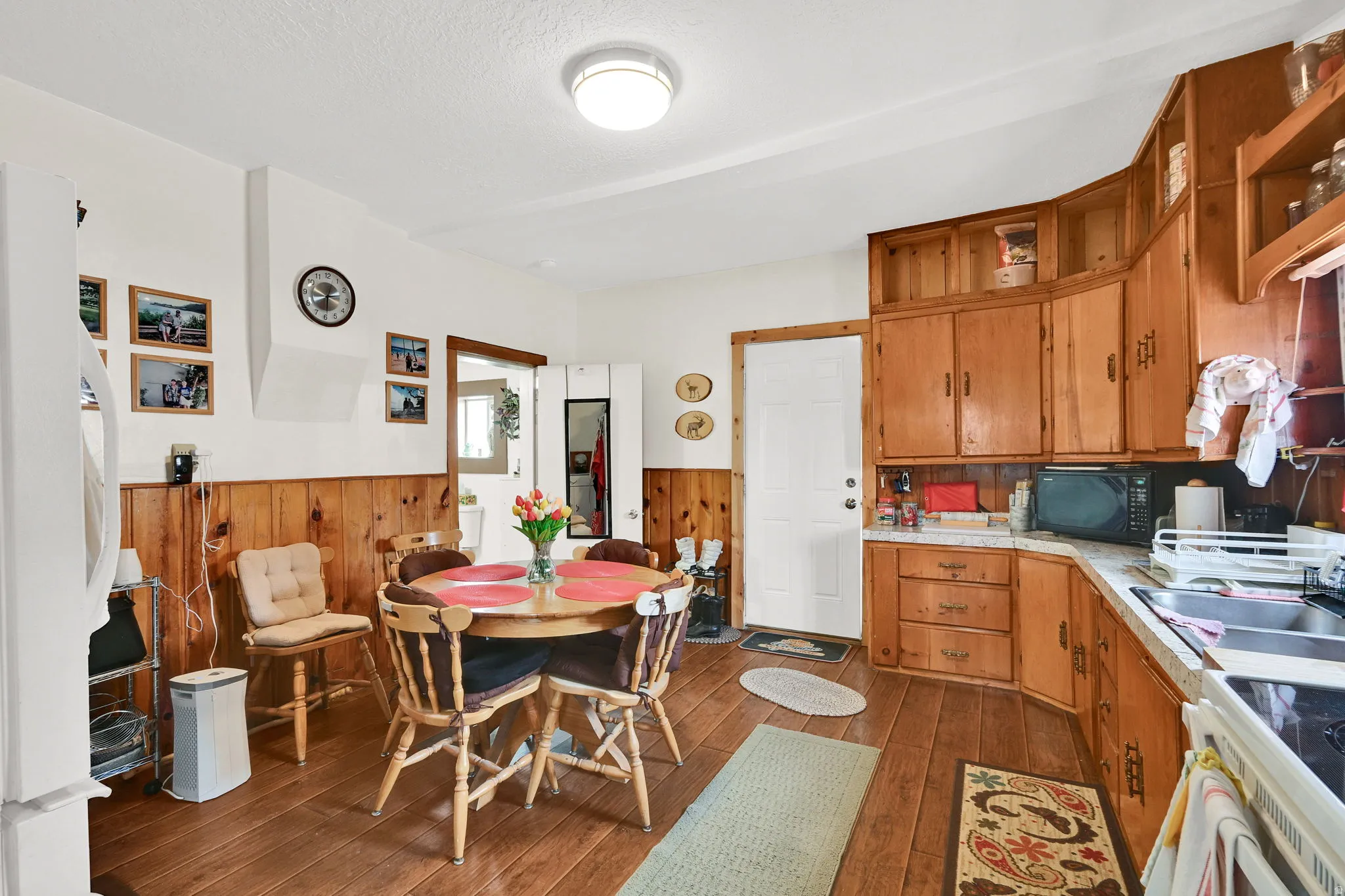 Kitchen featuring wood finish cabinets, wainscoting, dark wood-style flooring, white appliances, and wood walls