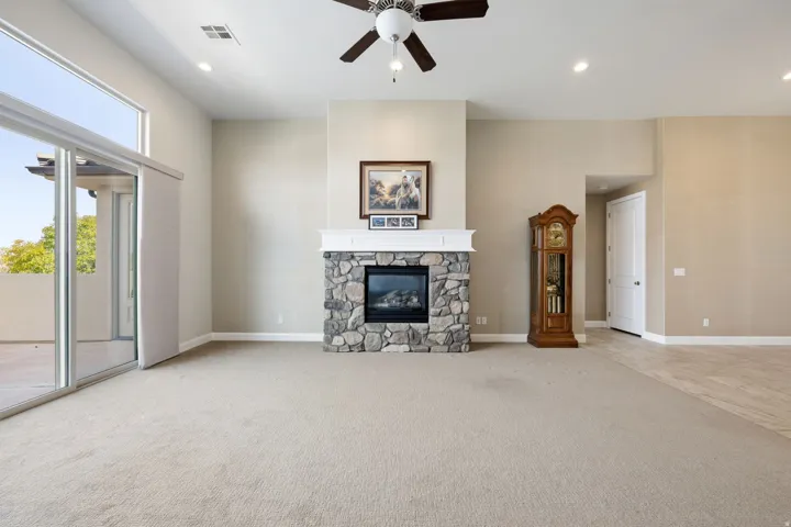 Living area with a ceiling fan, light carpet, a stone fireplace, and recessed lighting