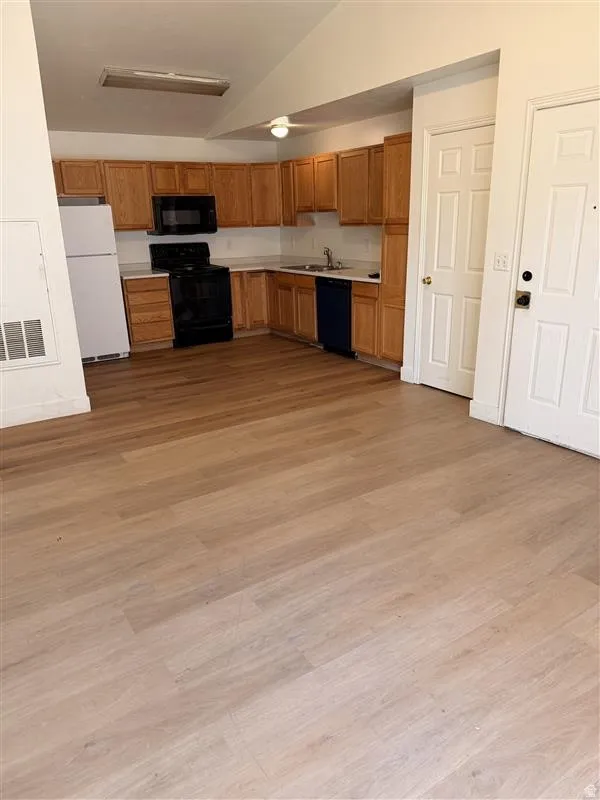 Kitchen with light countertops, vaulted ceilings, black appliances, wood finish cabinets, and light wood-style flooring