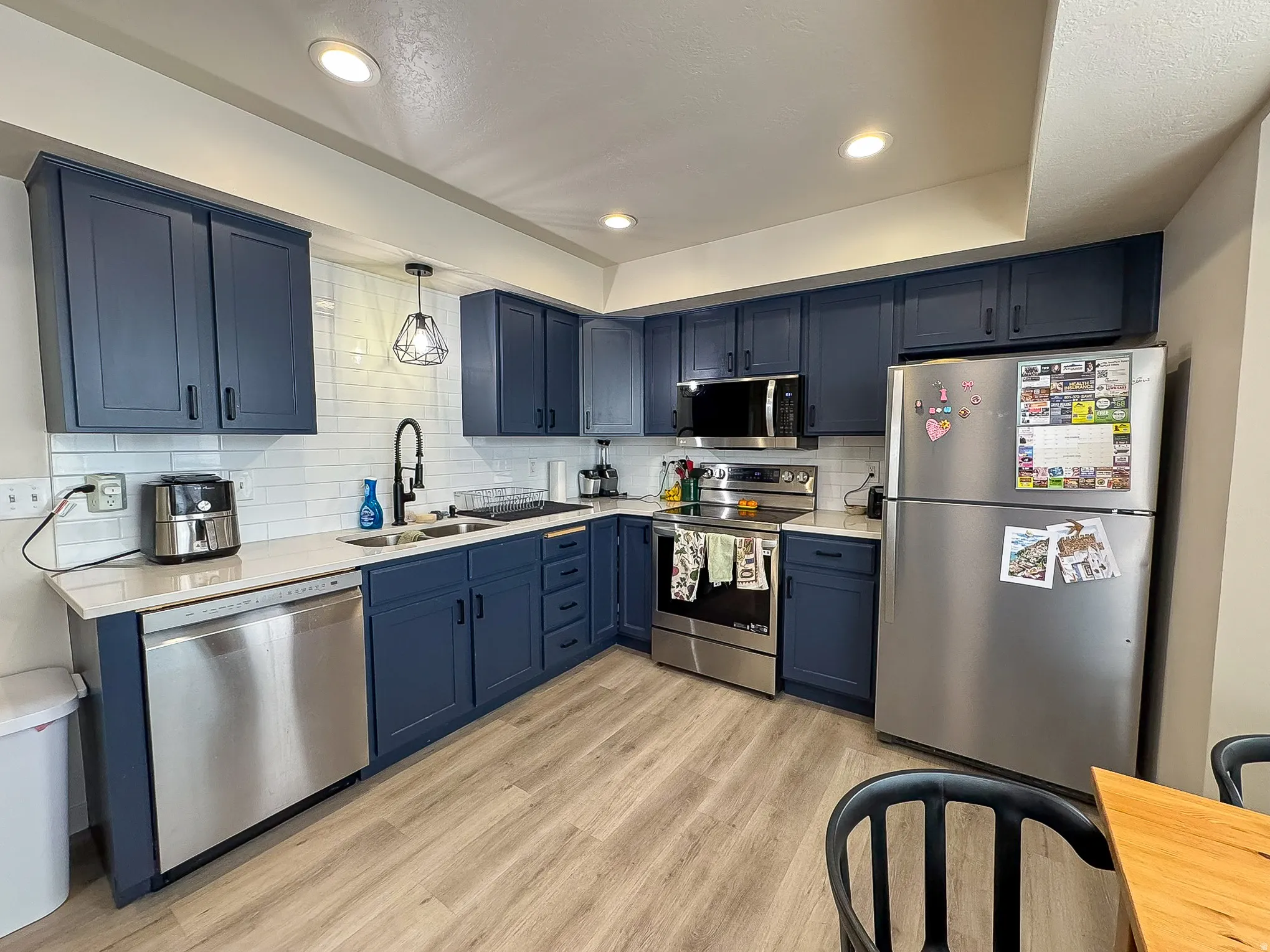 Kitchen featuring stainless steel appliances, blue cabinetry, backsplash, and light wood finished floors