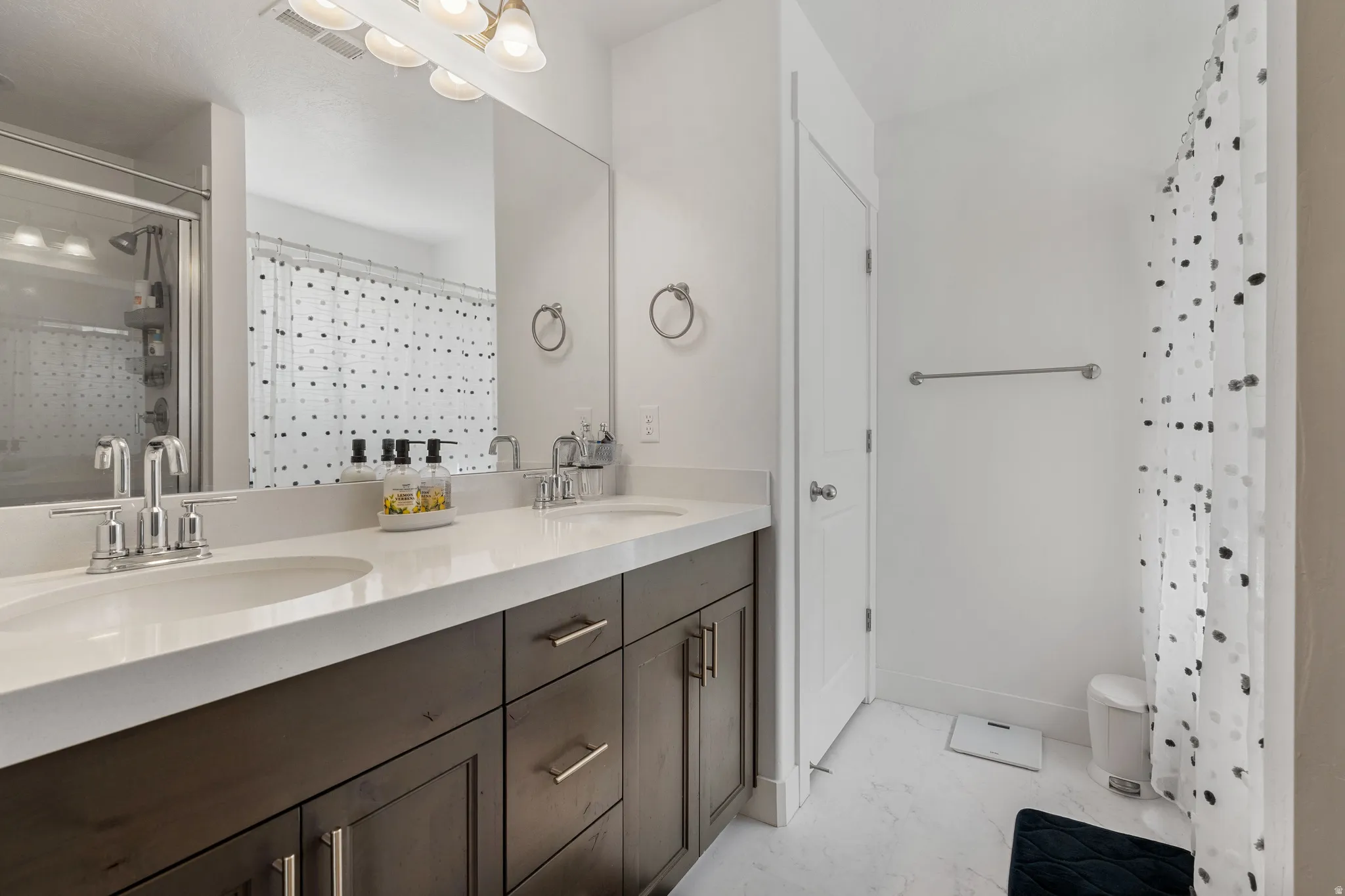Full bathroom with a shower stall, double vanity, and light marble finish flooring
