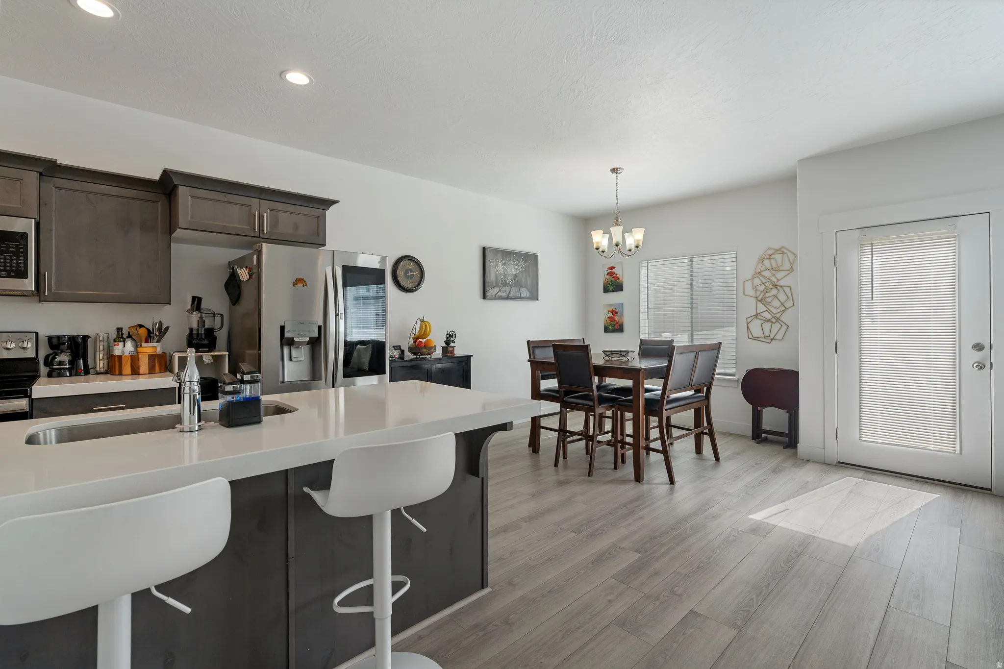 Kitchen featuring dark wood finish cabinets, stainless steel appliances, light wood-style flooring, a breakfast bar, and suspended lighting