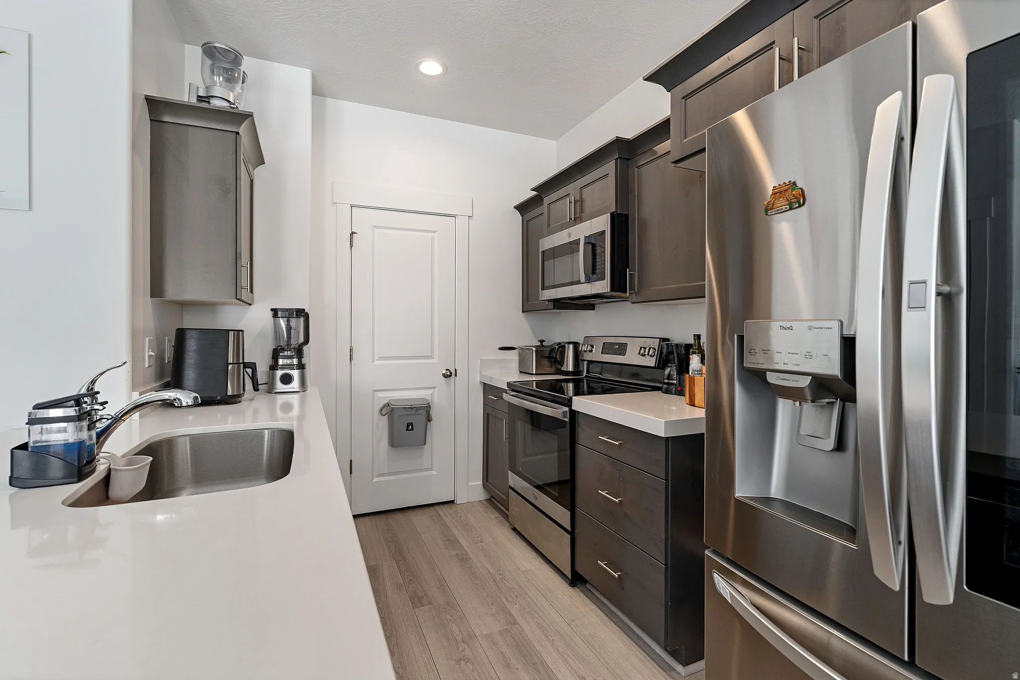 Kitchen featuring stainless steel appliances, light wood finished floors, dark wood finish cabinetry, and light stone countertops