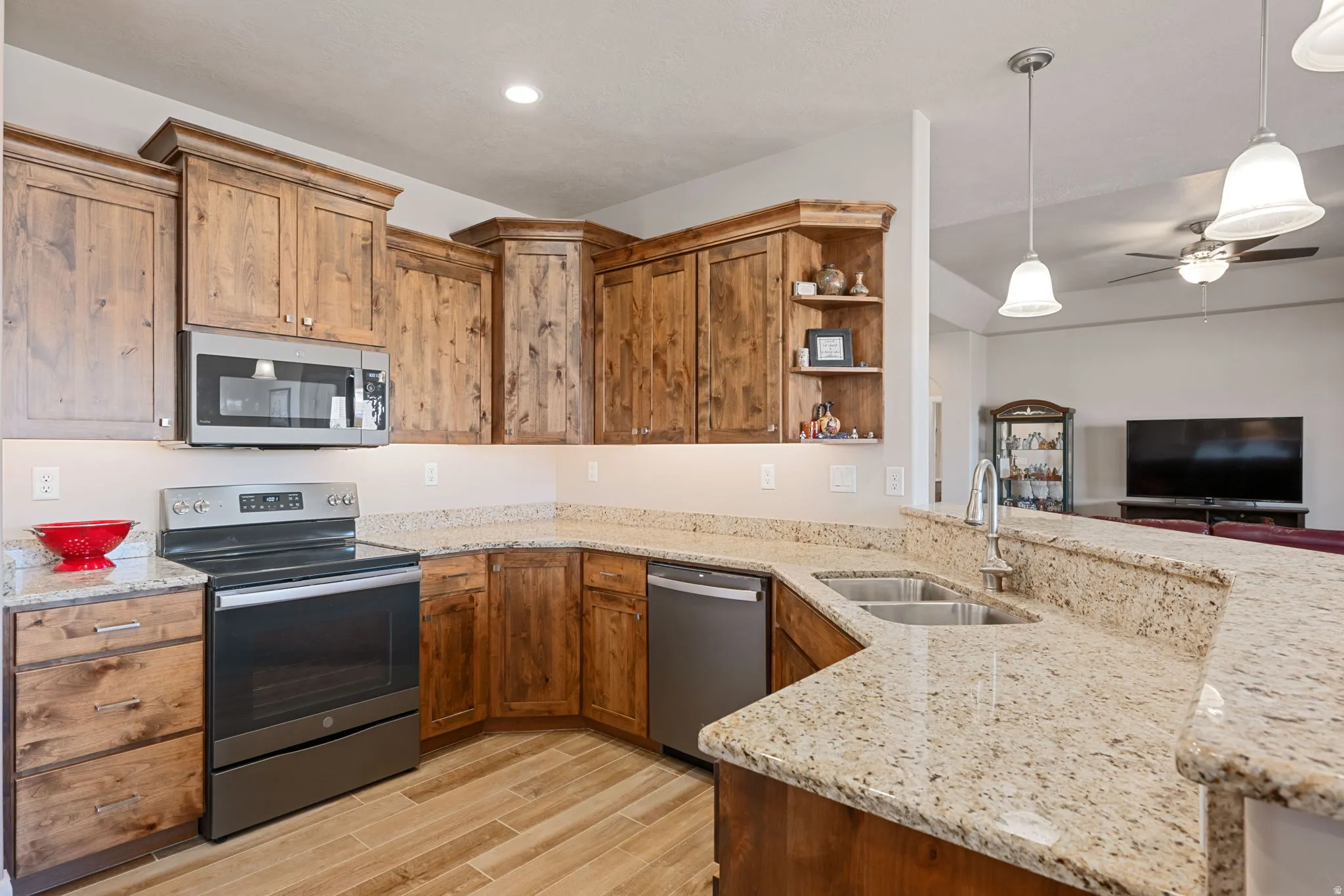 Kitchen featuring stainless steel appliances, light stone counters, a peninsula, a ceiling fan, and wood finish cabinets