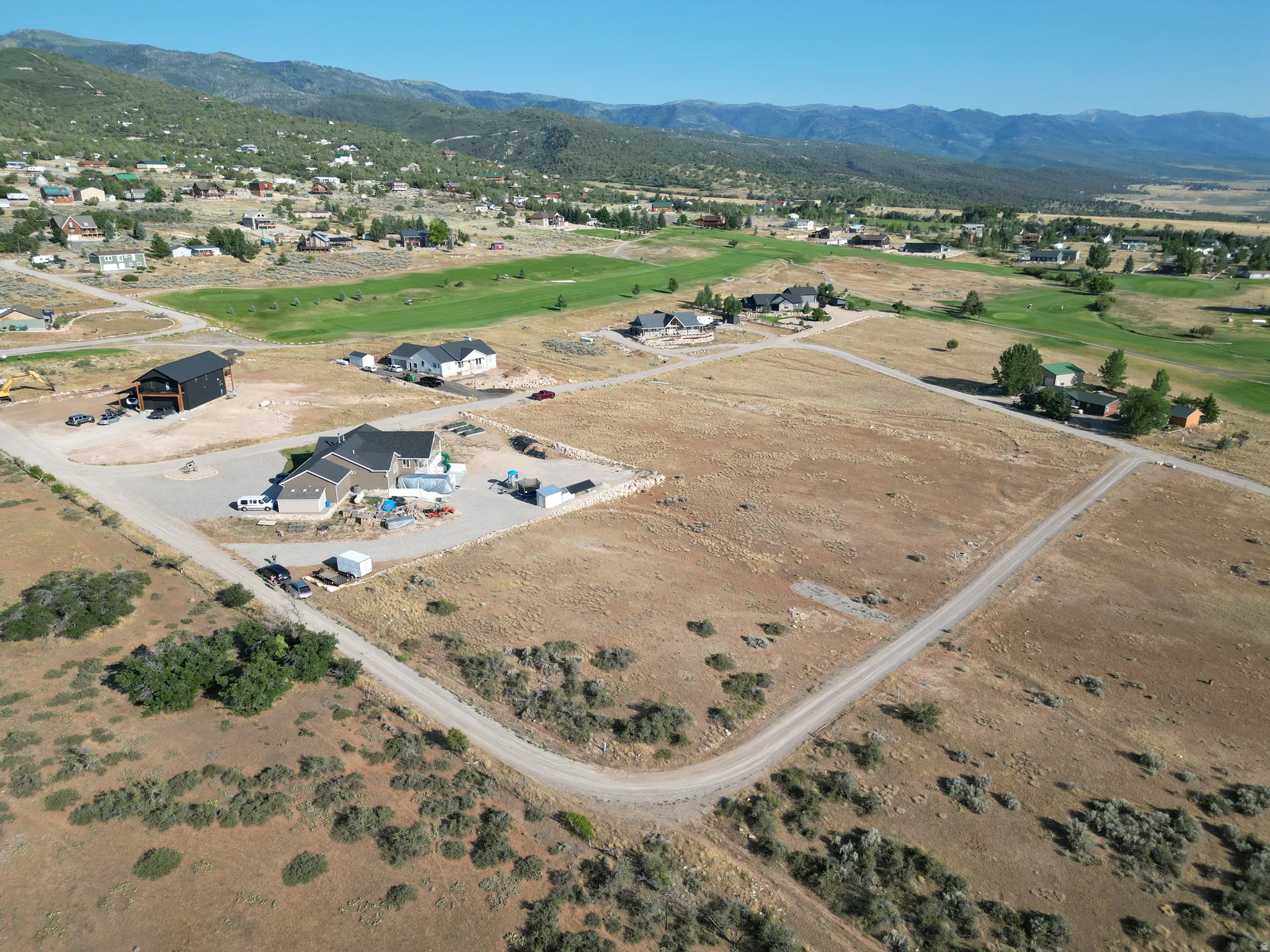 Aerial view of property and surrounding area featuring mountains, a local golf course, and nearby suburban area