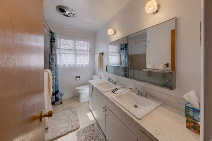 Full bathroom with double vanity, light tile patterned floors, and a shower with shower curtain
