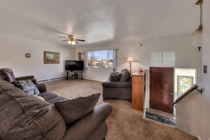 Living area featuring carpet flooring, ceiling fan, and baseboard heating