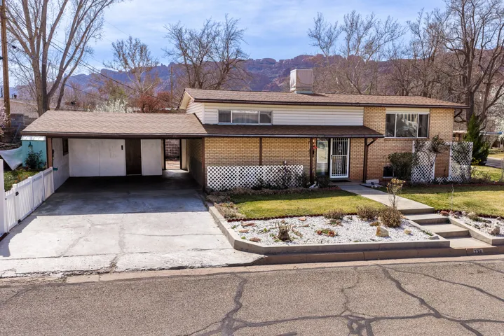 Tri-level home with brick siding, a carport, a front lawn, and concrete driveway