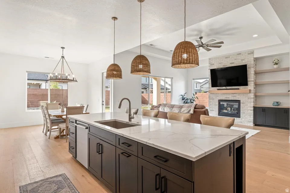 Kitchen with open floor plan, light wood-type flooring, a kitchen island with sink, a brick fireplace, and a raised ceiling