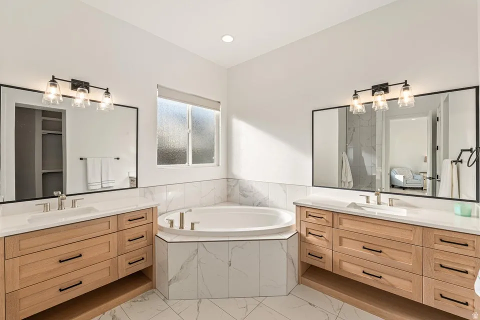 Bathroom with two vanities, a garden tub, and light marble finish floors