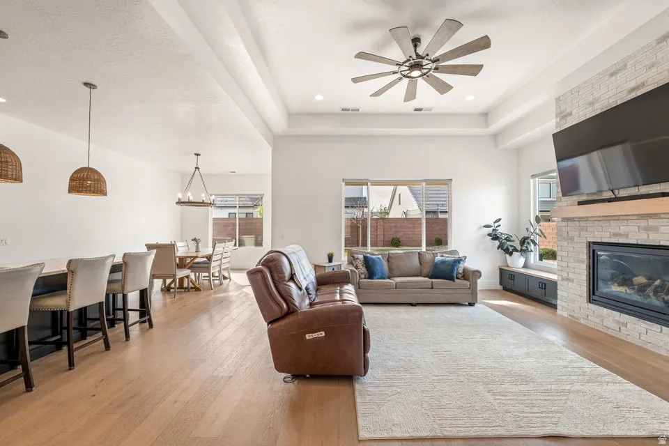 Living room featuring a fireplace, light wood finished floors, a tray ceiling, and ceiling fan