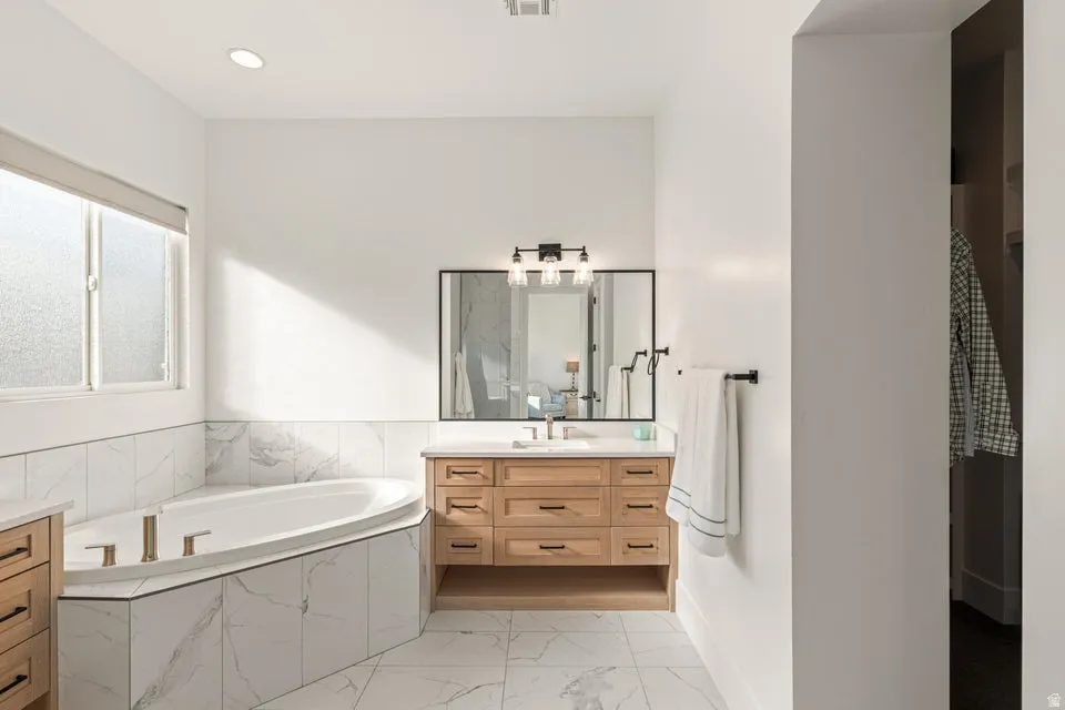Full bathroom featuring vanity, a garden tub, light marble finish flooring, and recessed lighting