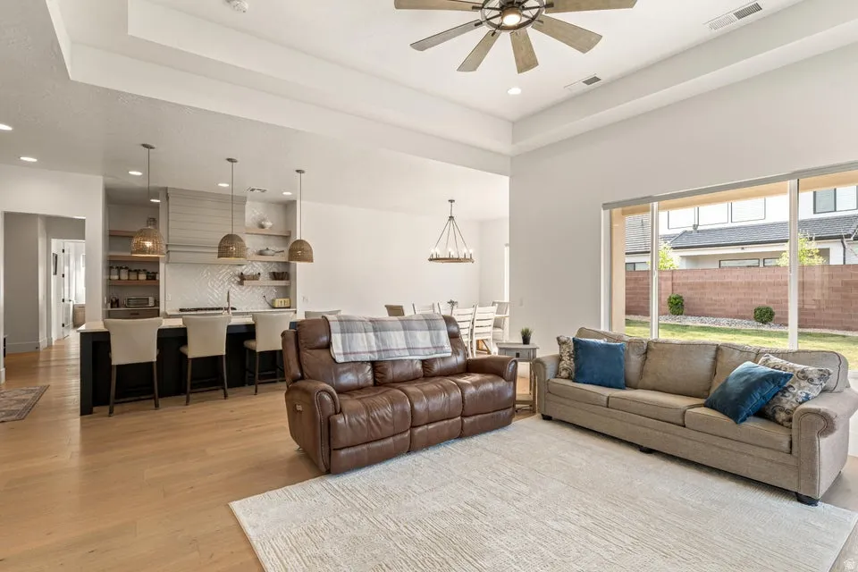 Living room with ceiling fan, light wood finished floors, recessed lighting, and a tray ceiling