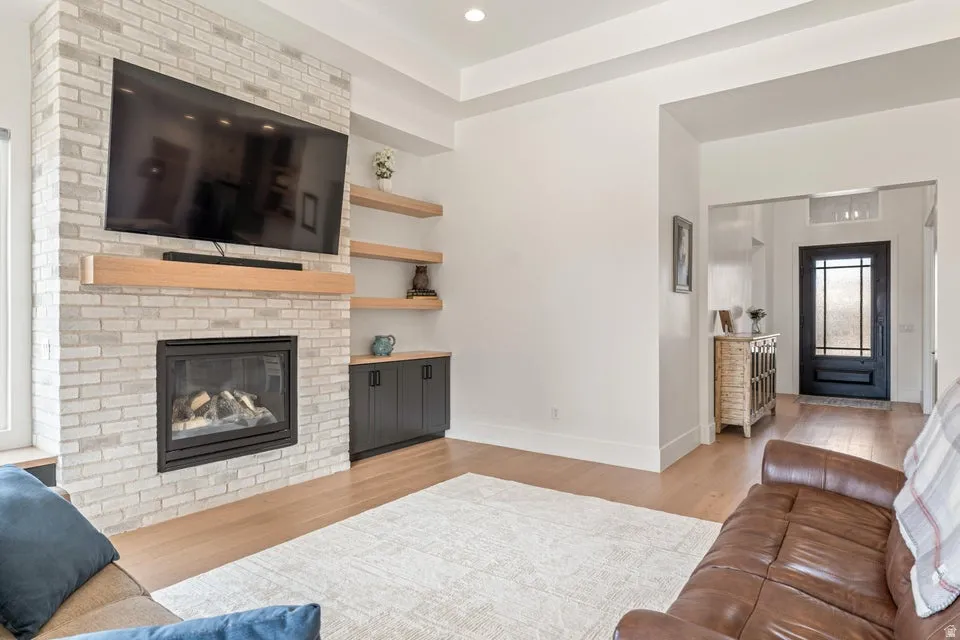 Living room with a brick fireplace, light wood-style floors, and recessed lighting