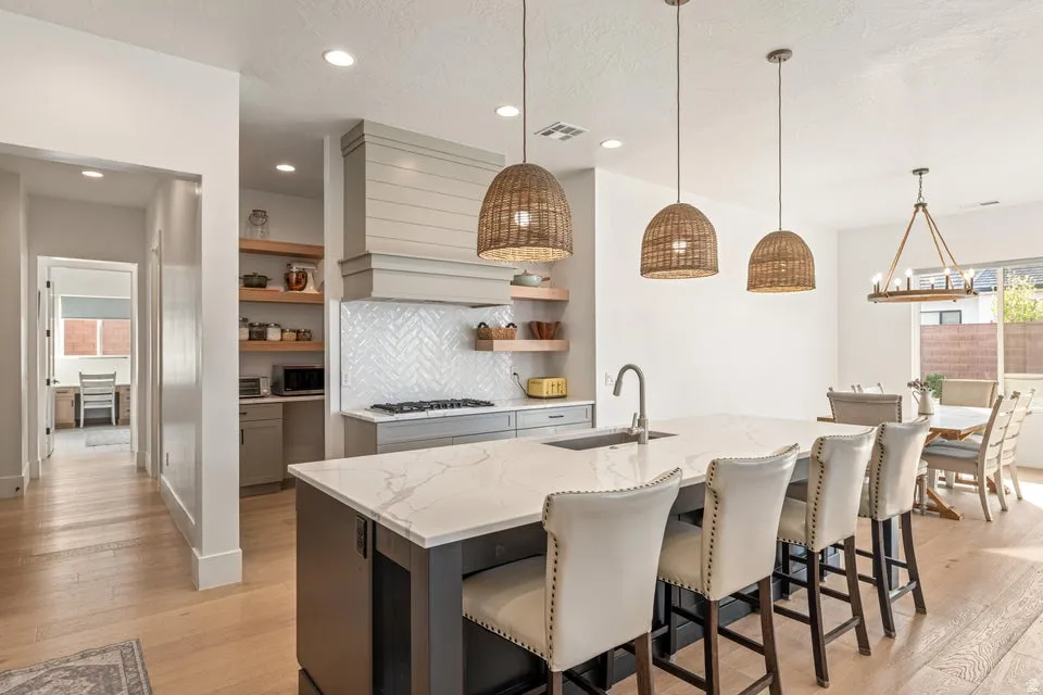 Kitchen with light stone countertops, a breakfast bar, open shelves, a kitchen island with sink, and hanging light fixtures