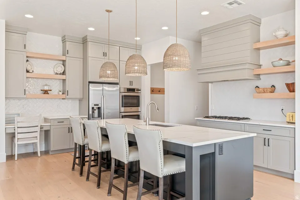 Kitchen with open shelves, backsplash, gray cabinets, stainless steel appliances, and light stone counters