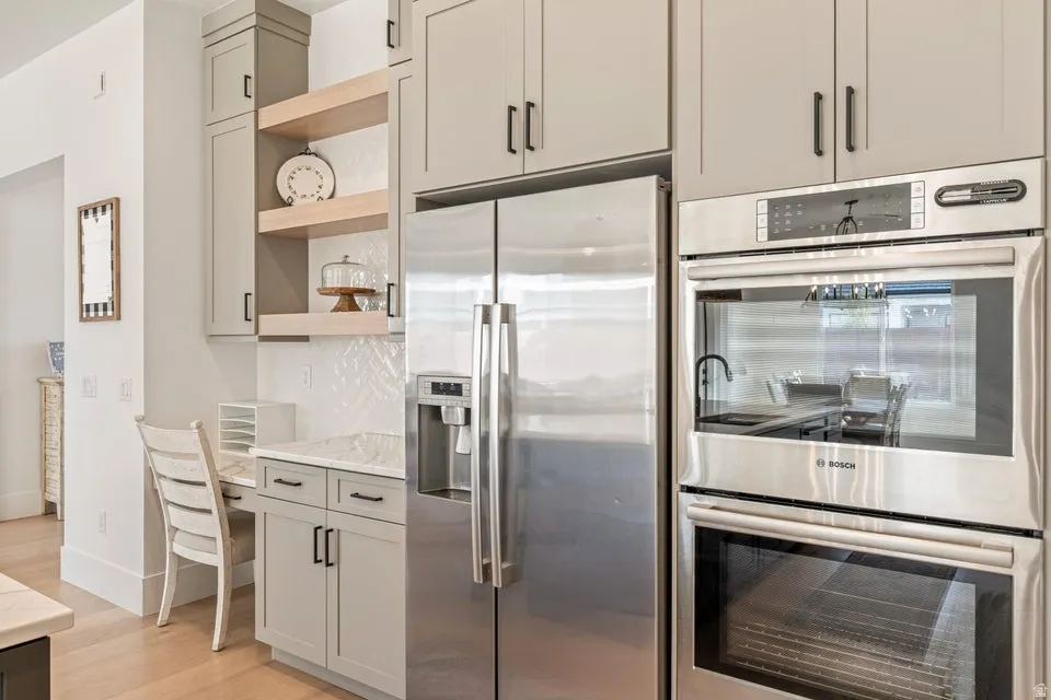 Kitchen featuring stainless steel appliances, open shelves, light wood finished floors, light stone counters, and gray cabinetry