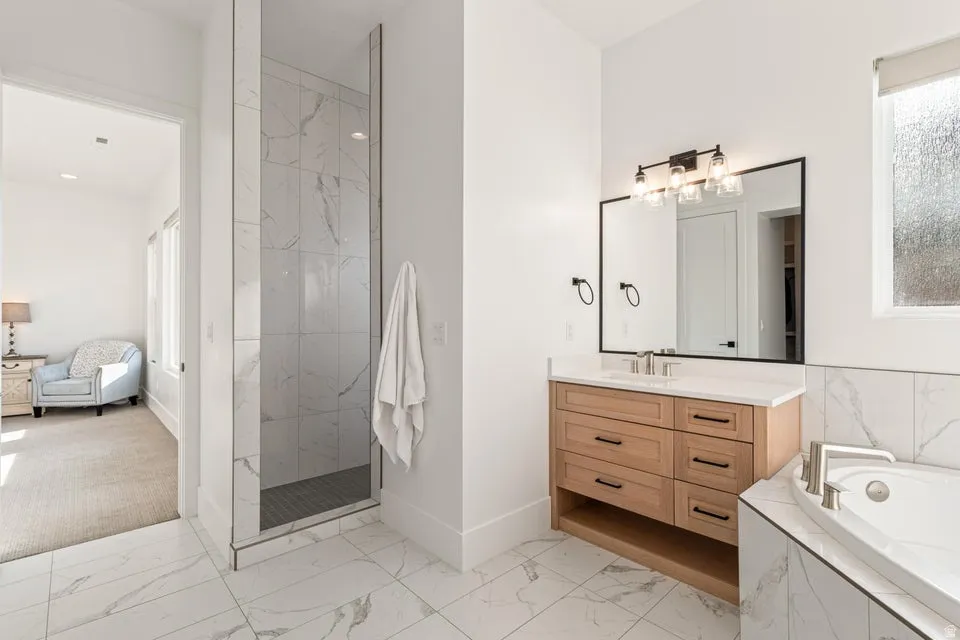 Bathroom with light marble finish flooring, vanity, a garden tub, and a marble finish shower