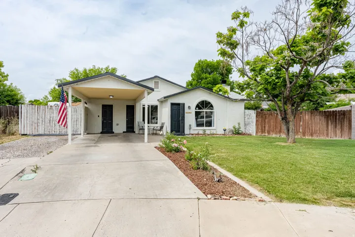 White stucco exterior featuring a covered carport, arched window, dark entry door, and a manicured front lawn