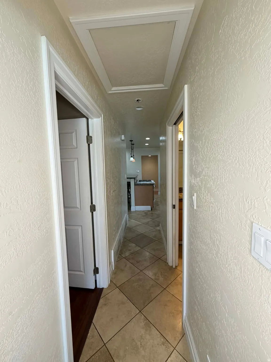 Corridor featuring a textured wall and light tile patterned floors
