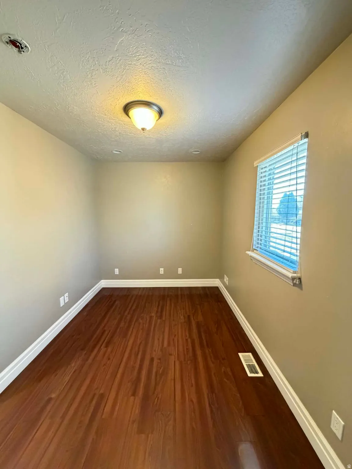Empty room featuring dark wood-type flooring and a textured ceiling