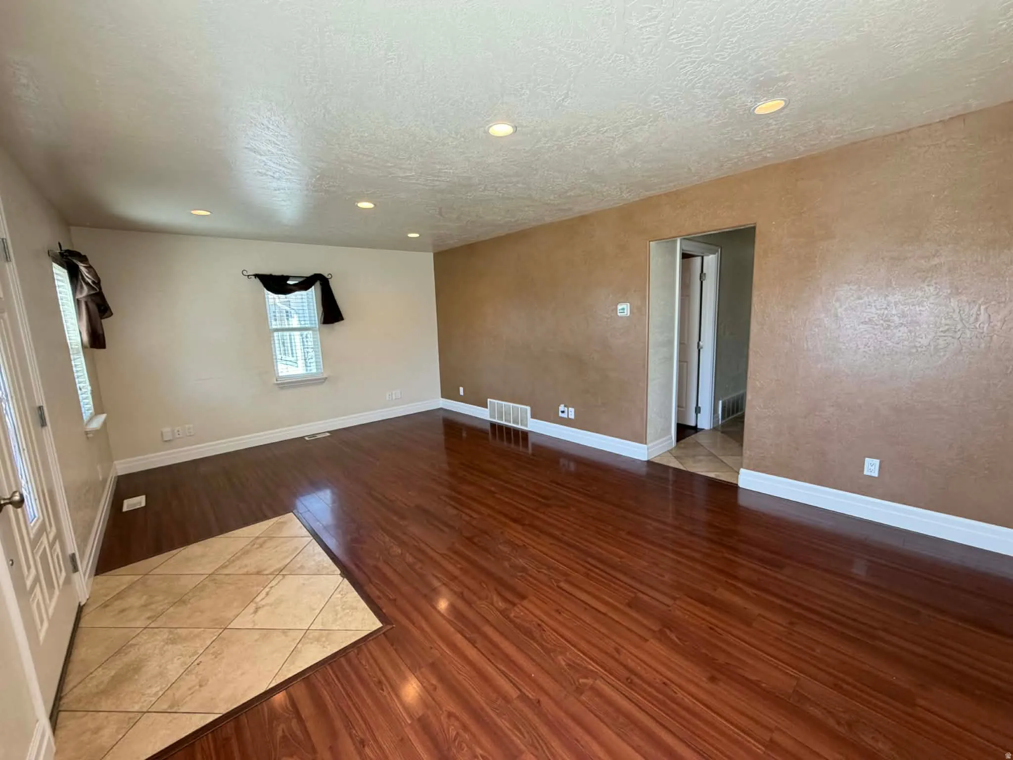 Empty room with dark wood-type flooring, a textured ceiling, a textured wall, and recessed lighting