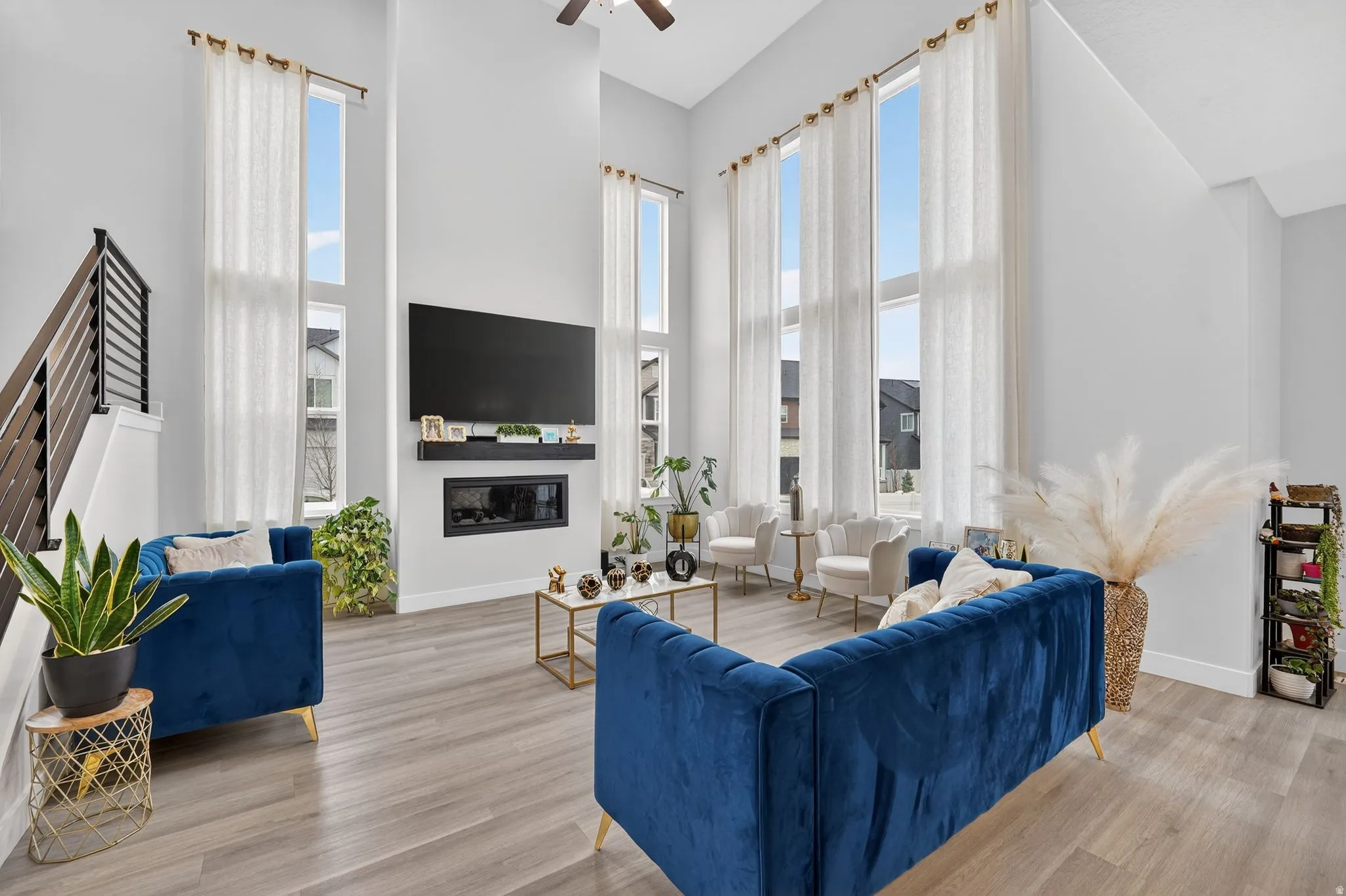 Living room featuring light wood finished floors, a high ceiling, a glass covered fireplace, and ceiling fan
