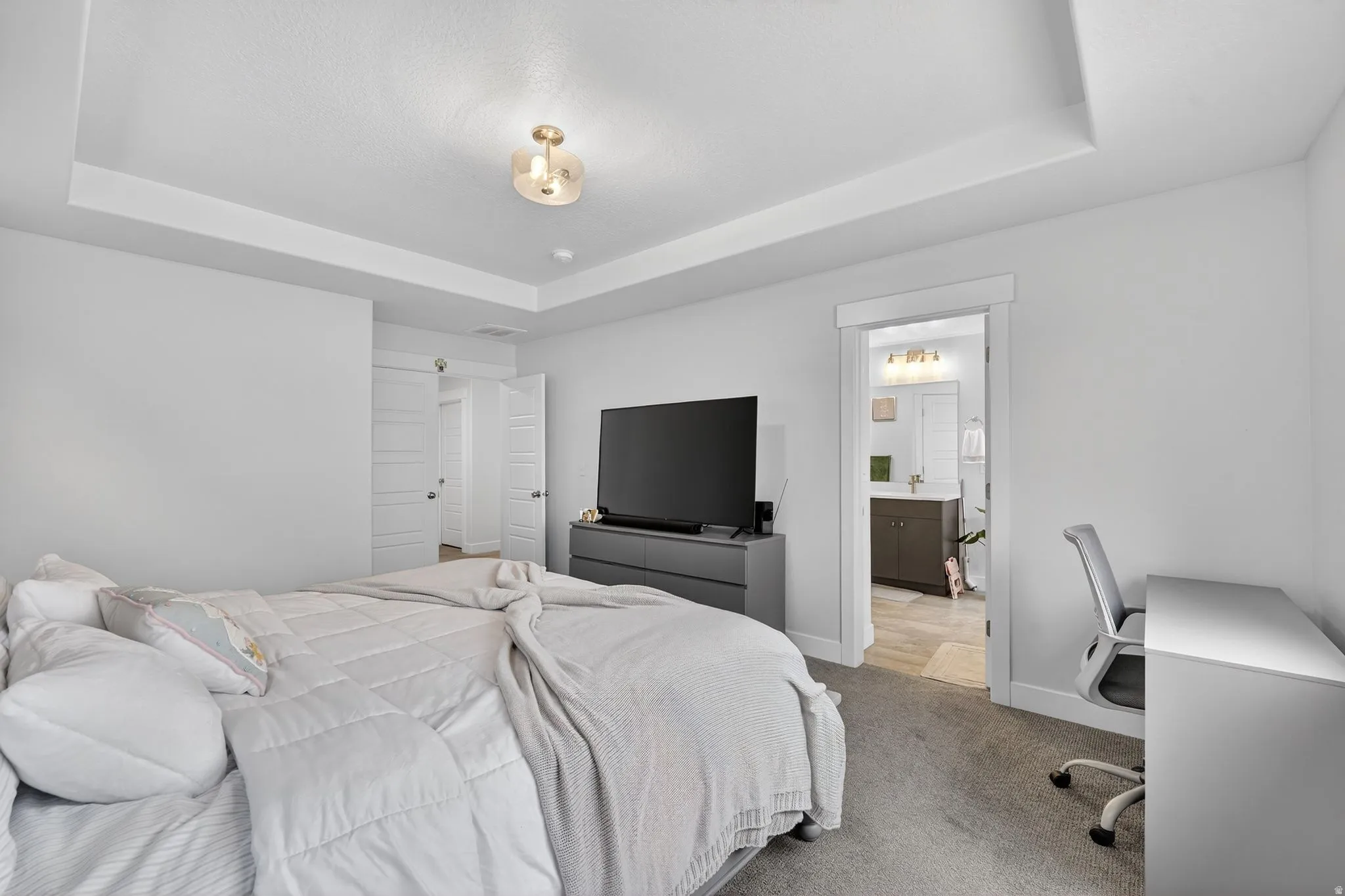 Bedroom with a raised ceiling, carpet flooring, an office area, and connected bathroom