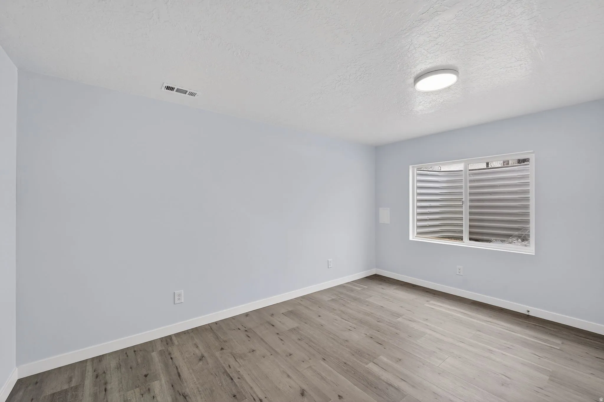 Empty room featuring a textured ceiling and light wood finished floors