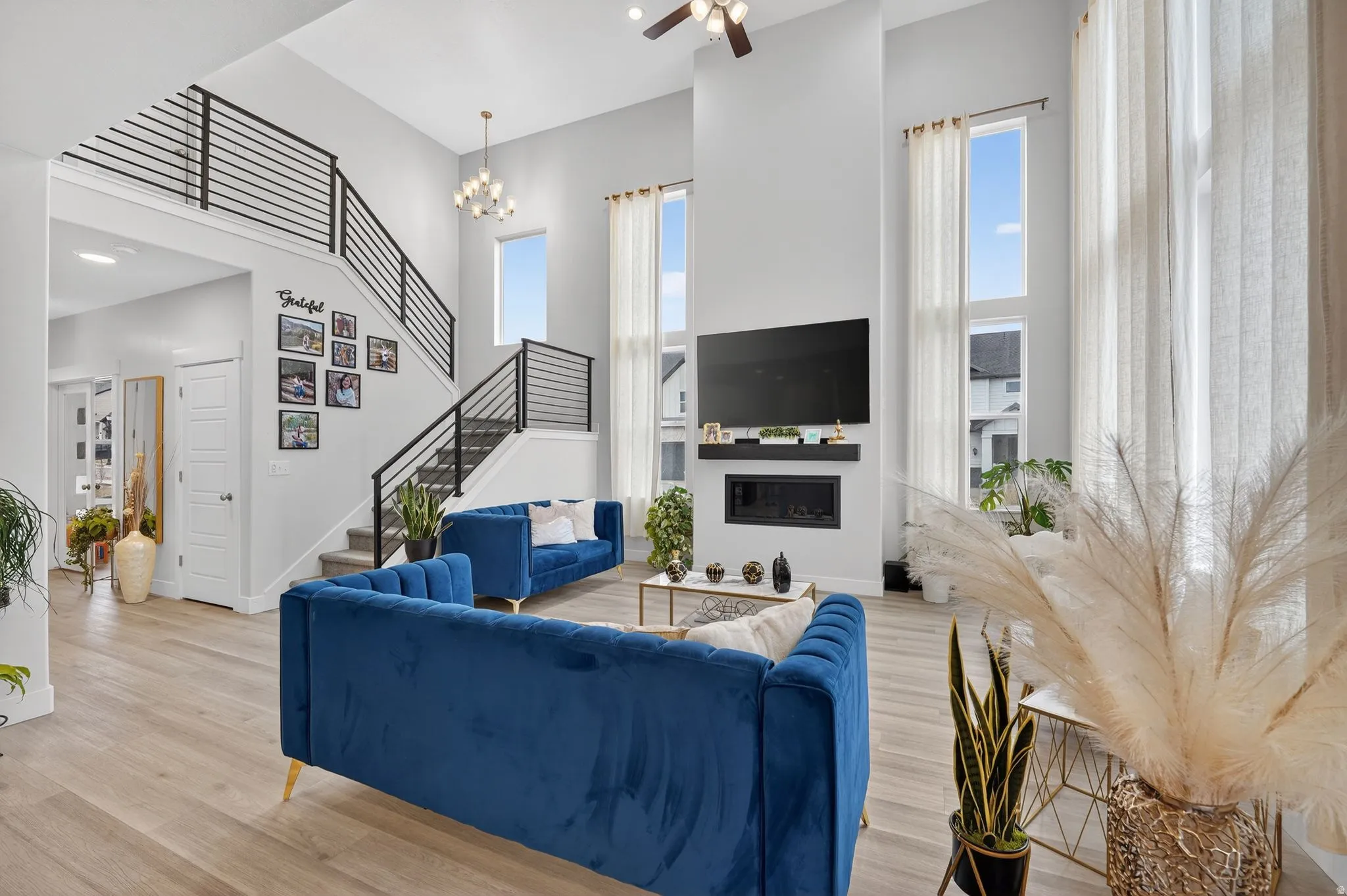 Living area with a high ceiling, light wood-style floors, hanging lights, and a glass covered fireplace