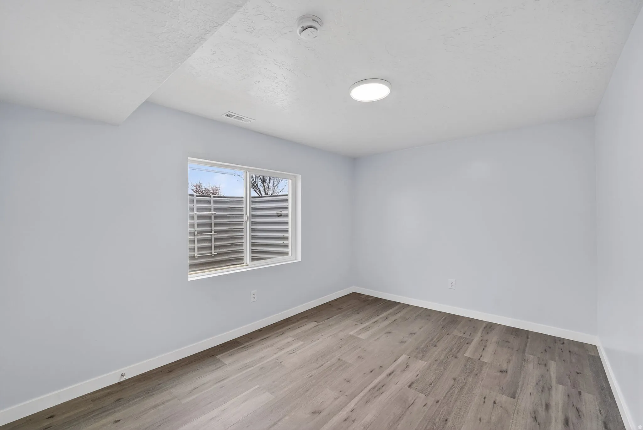Empty room with light wood-type flooring, a smoke detector, and a textured ceiling