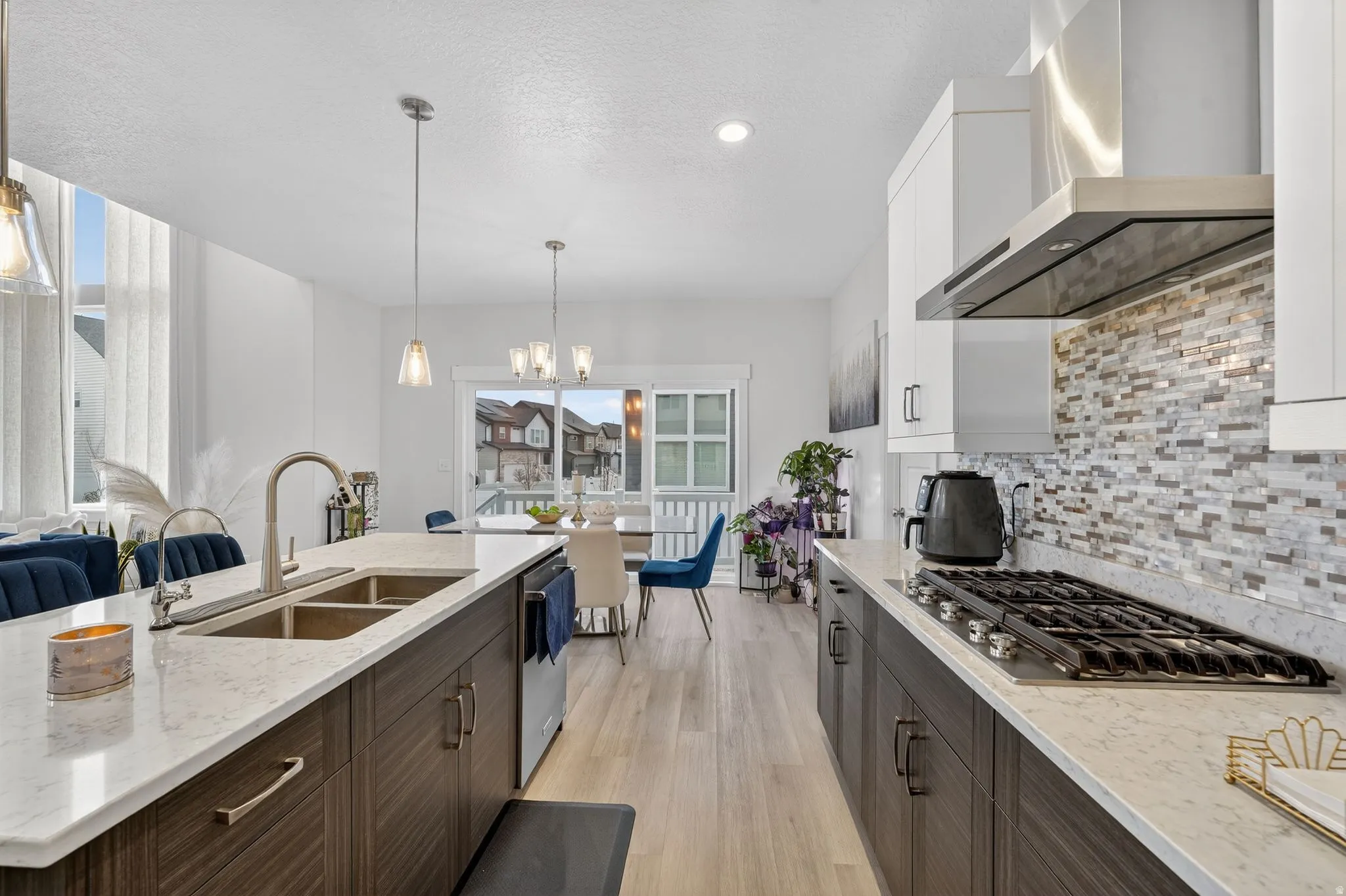 Two tone kitchen with light stone countertops, light wood-style flooring, stainless steel appliances, a chandelier, and dual tone cabinetry