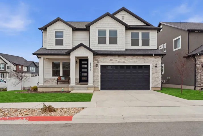 Craftsman inspired home with a front yard, covered porch, stone siding, and a garage
