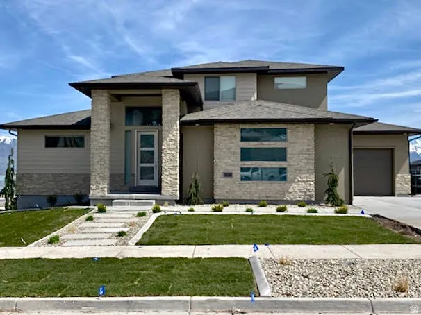 Prairie-style home featuring a front lawn, an attached garage, stone siding, and concrete driveway