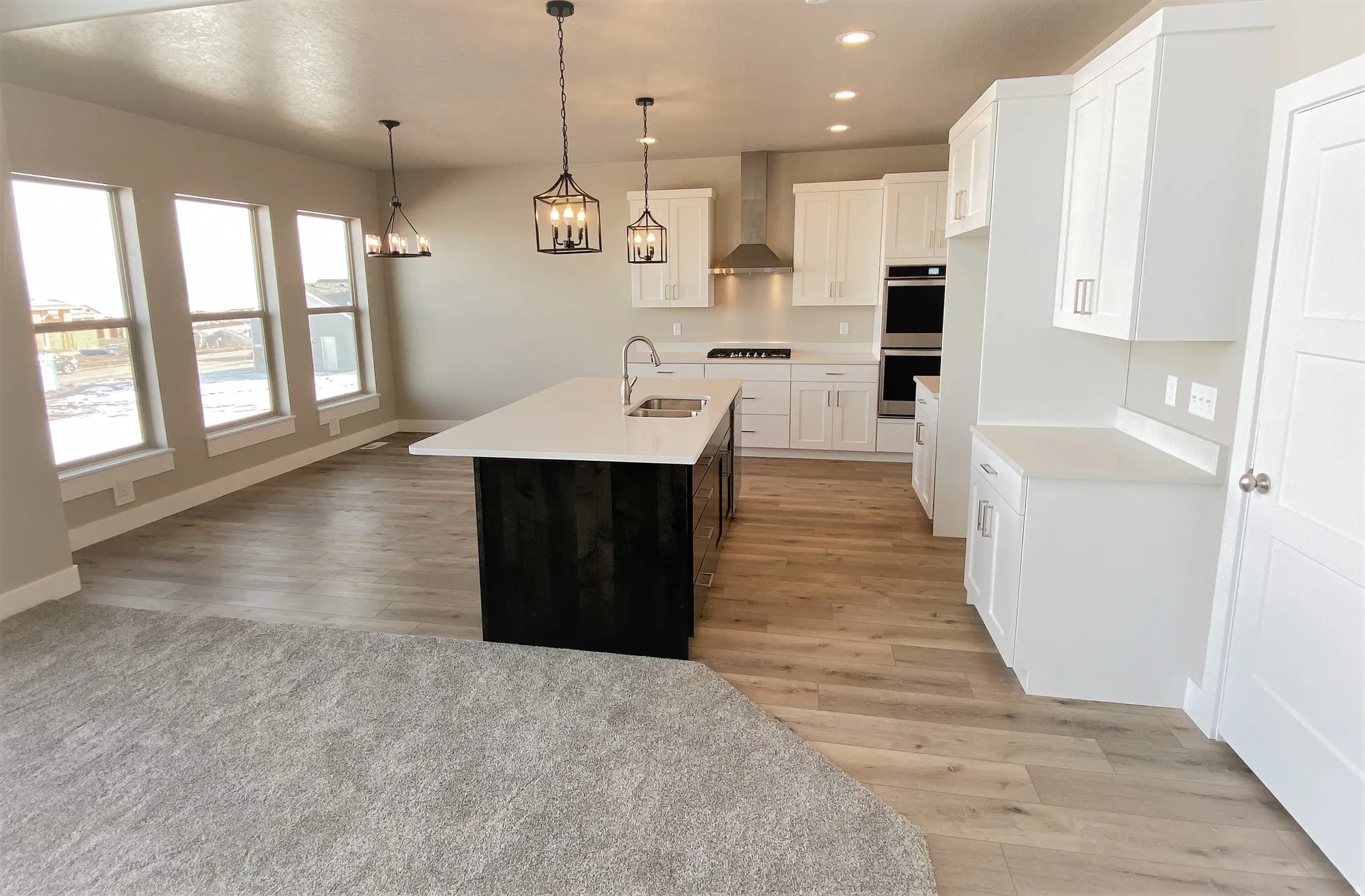 Dual tone kitchen with dual tone cabinetry, light wood-type flooring, a center island with sink, stainless steel double oven, and pendant lighting