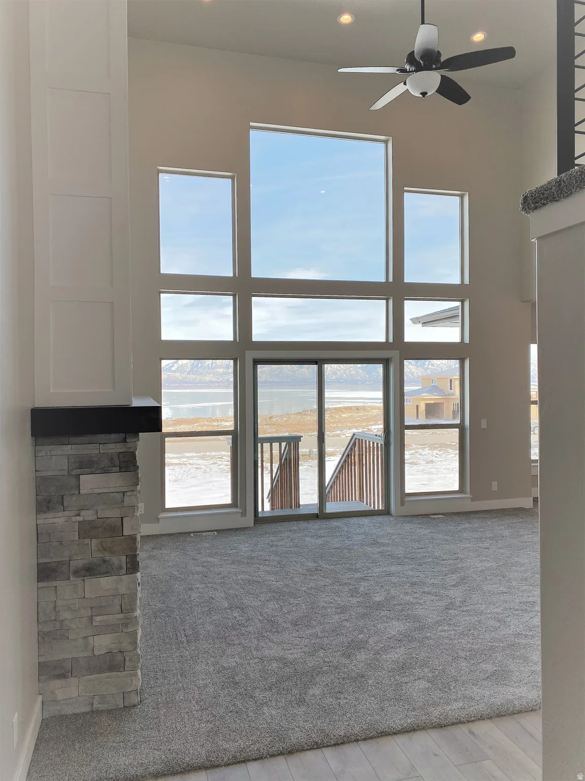 Unfurnished living room featuring a high ceiling, carpet, ceiling fan, and a water view