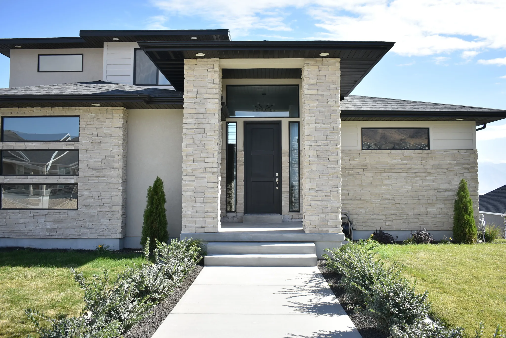 View of exterior entry with a lawn, stone siding, stucco siding, and roof with shingles